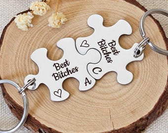 May include: Two silver-colored metal puzzle piece keychains with split rings. Each piece is engraved with the text "Best Bitches," a small heart symbol, and the letters "A" and "C" respectively, designed to interlock together.