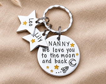 May include: A silver-toned metal keychain featuring a round disc engraved with the text NANNY we love you to the moon and back, accompanied by a rocket, moon, and star icons. Two star-shaped charms are attached, each engraved with the names Leo and Lily.