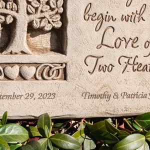 May include: A white stone garden plaque with a carved tree and two hearts. The plaque reads "begin with the Love of Two Hearts" and "September 29, 2023" and "Timothy & Patricia Jones".
