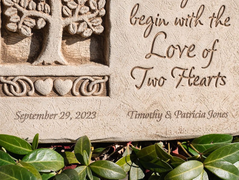 May include: A white stone garden plaque with a carved tree and two hearts. The plaque reads "begin with the Love of Two Hearts" and "September 29, 2023" and "Timothy & Patricia Jones".