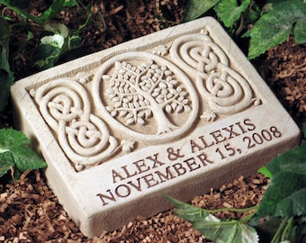 May include: A light gray stone garden marker with a Celtic knot design and a tree of life carving. The text "Alex & Alexis November 15, 2008" is engraved on the stone.