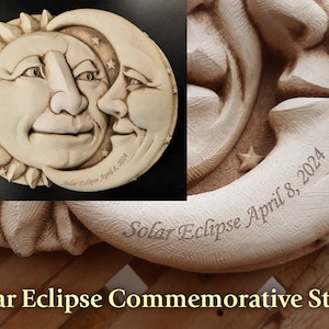 May include: A white ceramic commemorative stone with a sculpted sun and moon design. The sun and moon have faces and the moon is a crescent shape. The stone is engraved with the text "Solar Eclipse April 8, 2024".