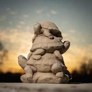 May include: A stack of three stone turtle figurines, each with a detailed shell and head, arranged in a pyramid shape. The turtles are a light beige color and are set against a blurred background of a sunset sky.