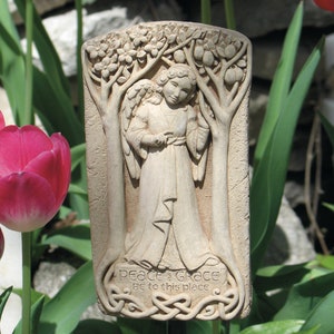 May include: A white ceramic garden stake with a relief sculpture of an angel standing in a tree. The stake has the text "Peace & Grace Be to this place" at the bottom.