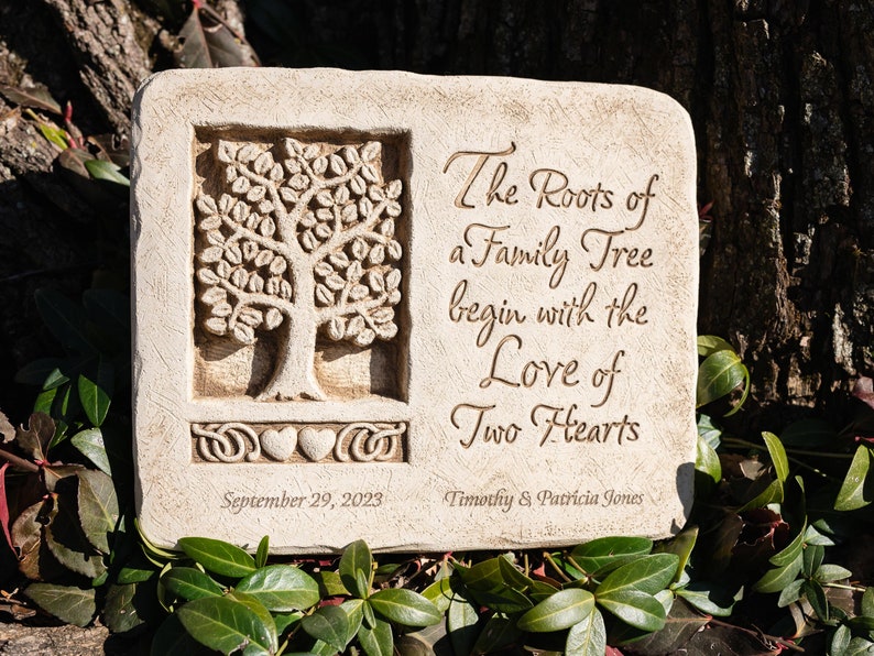 May include: A beige stone garden plaque with a carved tree design and the inscription "The Roots of a Family Tree begin with the Love of Two Hearts". The plaque also includes the date "September 29, 2023" and the names "Timothy & Patricia Jones".