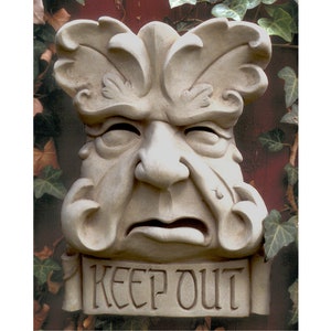 May include: A white stone sculpture of a face with a leafy design around the head. The face is frowning and has a sign that says "Keep Out".