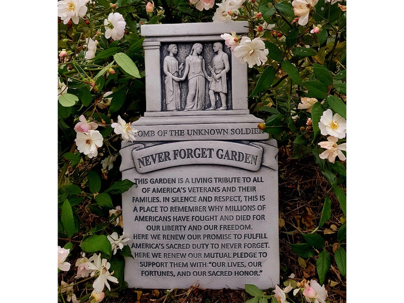 May include: A grey stone memorial with the words "Never Forget Garden" and a quote about honouring veterans and their families. The memorial features a sculpted image of three figures, likely representing soldiers.