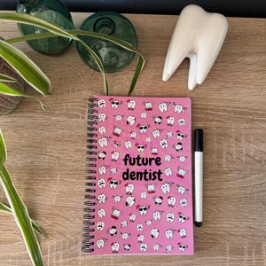 K&ouml;nnte beinhalten: Rosa Notizbuch mit Spiralbindung, einem wei&szlig;en Zahndesign und dem Text "future dentist".