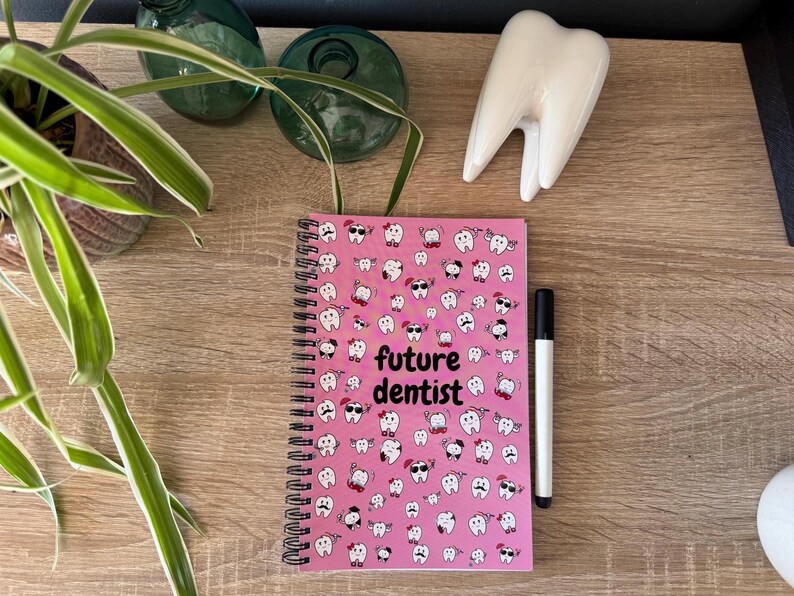 K&ouml;nnte beinhalten: Rosa Notizbuch mit Spiralbindung, einem wei&szlig;en Zahndesign und dem Text "future dentist".