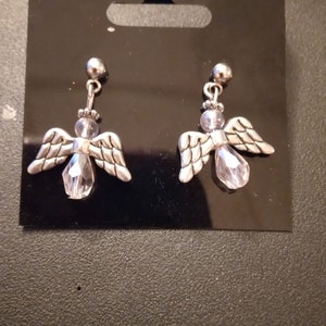 May include: A pair of silver angel earrings with clear crystal accents. The earrings are on a black card.