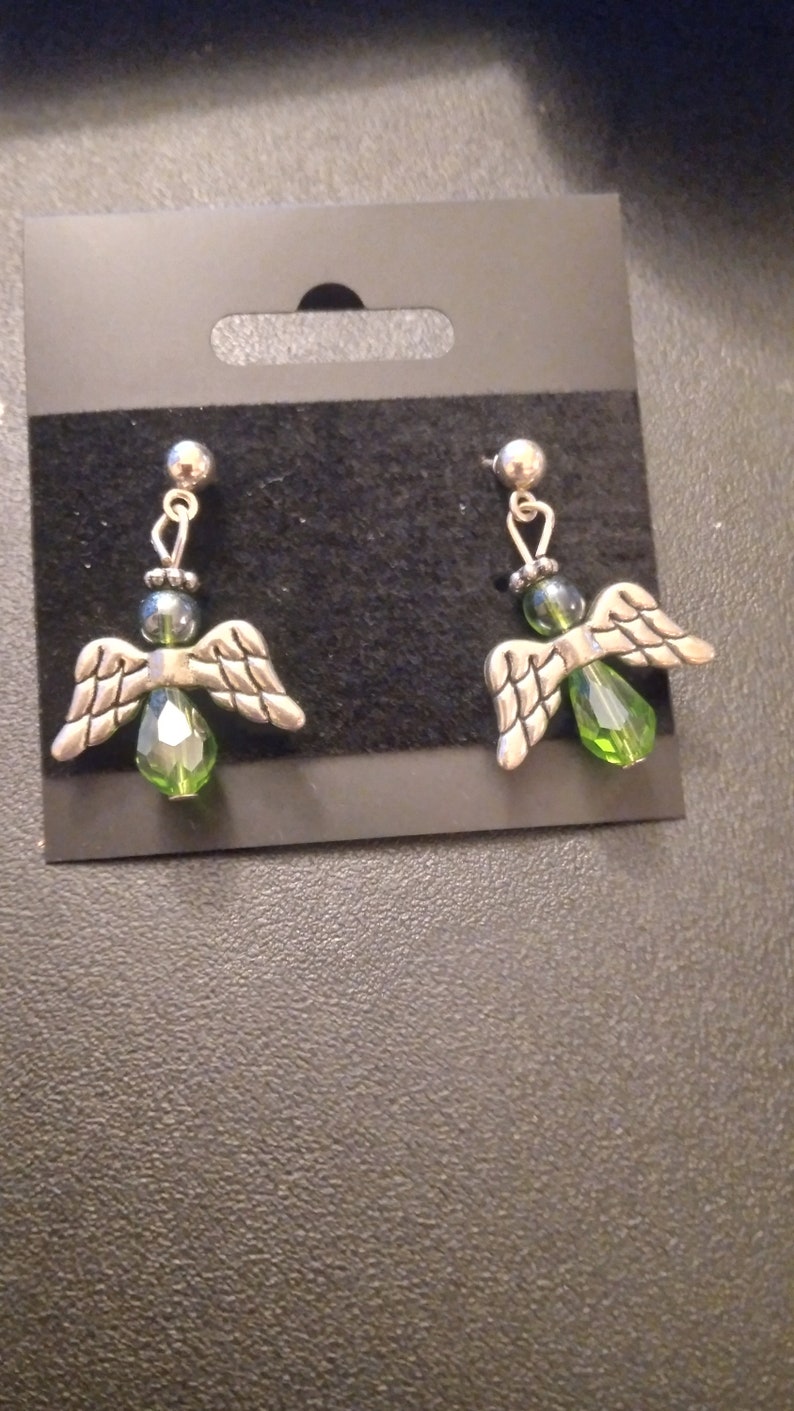May include: A pair of silver angel wing earrings with green crystal accents.