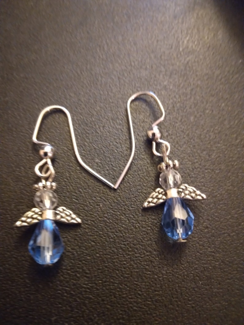 May include: A pair of silver angel dangle earrings with blue crystal teardrop accents.