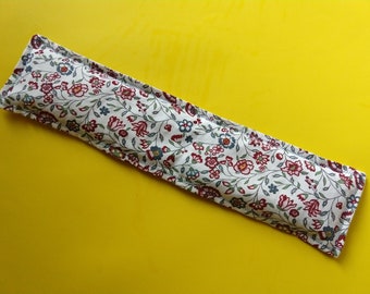 May include: A white fabric heating pad with a floral pattern in shades of red, blue, and green. The pad is rectangular and has a seam down the center.