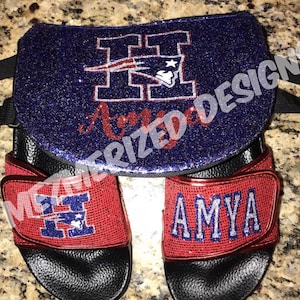 May include: A set of red and black slides with a blue and white letter H and the name AMYA in silver glitter. The slides are paired with a blue and black glittery bag with the same letter H and the name AMYA in red glitter.