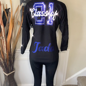 May include: Black long-sleeved jersey with blue glitter lettering that says "Class of 21" and "Jada" on the back.