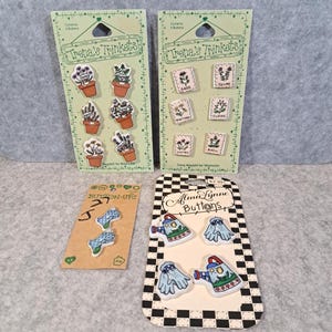May include: A collection of decorative buttons, including packs with plant designs and the text "Trena's Trinkets." Other packs feature blue and white buttons, and watering can and glove designs with the text "Alma Lynne Buttons."