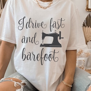 Puede incluir: Camiseta blanca con el texto "I drive fast and barefoot" y un gráfico de máquina de coser negra.