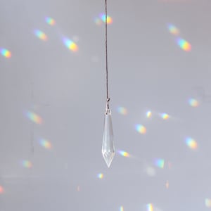 May include: A crystal prism hanging from a copper ring on a string, casting rainbow light on a white wall.
