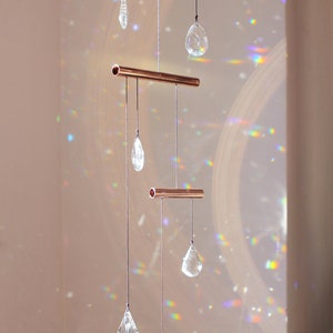 May include: A copper crystal suncatcher with five clear crystal drops hanging from three copper bars. The suncatcher casts rainbows on the wall behind it.