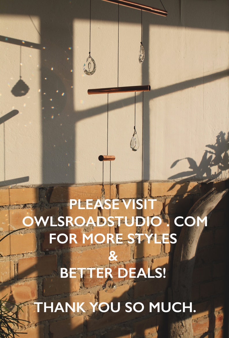 May include: A copper and crystal mobile with three teardrop-shaped crystals hanging from a copper bar. The mobile is hanging from a ceiling against a brick wall. The text "PLEASE VISIT OWLSROADSTUDIO.COM FOR MORE STYLES & BETTER DEALS! THANK YOU SO MUCH." is printed below the mobile.