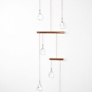 May include: A copper and crystal mobile with six clear crystal drops hanging from three copper bars. The mobile is suspended from a copper triangle.