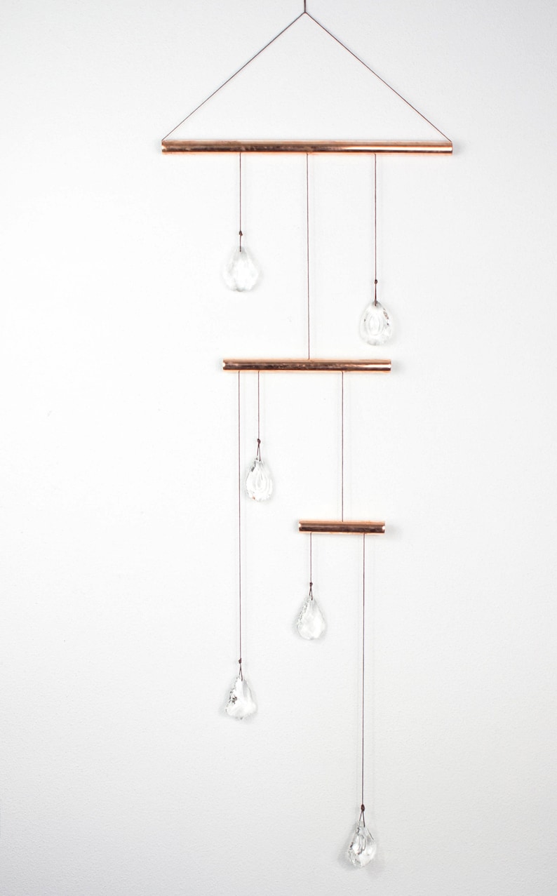 May include: A copper and crystal mobile with six clear crystal drops hanging from three copper bars. The mobile is suspended from a copper triangle.