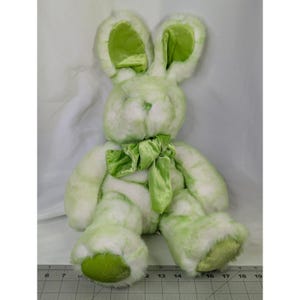 May include: A plush Easter bunny in shades of green and white. The bunny has long ears with green inner linings, a green bow, and green accents on its feet. The soft toy is designed to sit upright.