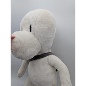 May include: A large, plush white stuffed animal with a rounded head, large snout, and black eyes. It has a gray strap around its neck. The toy is made of soft, fuzzy material.