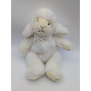 May include: A plush, white lamb stuffed animal with a cream-colored face, ears, and feet. The lamb has a white ribbon tied around its neck. The lamb is sitting upright with its arms and legs extended.