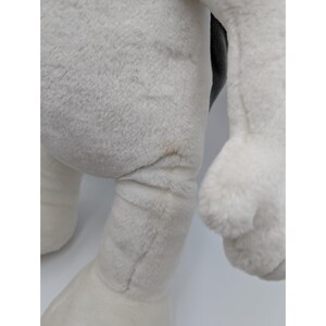 May include: Close-up of a plush toy's leg and arm. The toy is primarily white with a gray area and a black section. The plush material appears soft and fluffy. There is a small brown stain on the leg.