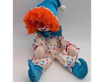 May include: A vintage clown doll with a blue hat and shoes, orange hair, and a polka-dot outfit. The doll has a red nose and a white face. The clown is sitting down with its legs extended.