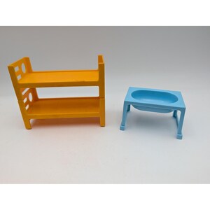 May include: A bright yellow plastic bunk bed frame with side ladder cutouts and a light blue plastic sink or basin stand with four legs. Both items are miniature toy furniture pieces designed for small-scale play sets and display.