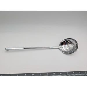 May include: A stainless steel skimmer with a long handle and a perforated, rounded bowl. The handle is approximately 12 inches long, and the bowl is about 4 inches in diameter. The skimmer is designed for straining liquids or removing solids from cooking pots.