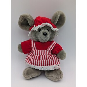May include: A plush gray mouse wearing a red dress with white stripes and a matching bonnet. The dress has white straps and a white eyelet lace trim. The mouse has large gray ears and a black nose. A cute stuffed animal.