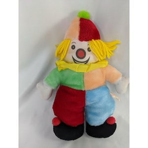 May include: A colorful plush clown doll with a patchwork design. The clown has a red, orange, and pink hat with a green pom-pom, yellow yarn hair, and a smiling face. The body is divided into sections of green, orange, red, and blue.