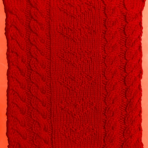 Puede incluir: Tejido de punto rojo con un patrón de punto trenzado. El tejido tiene una superficie texturizada y está hecho de un material suave y cálido.
