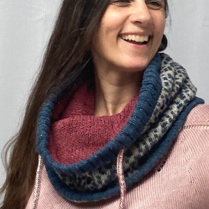 May include: A woman wearing a pink sweater with a blue, white, and pink cowl neck scarf. The scarf has a geometric pattern.