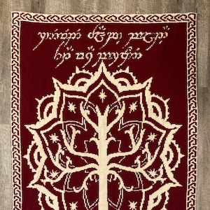 May include: A red knitted tapestry featuring a white tree of life design and a white inscription in Elvish script that reads "Yavanna's gift to the world of men".