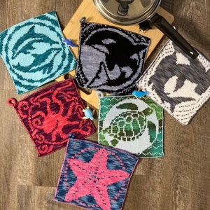 Può includere: Sei presine a maglia con diversi disegni di creature marine. I disegni includono una stella marina, un polpo, una tartaruga, una balena, un delfino e un cavalluccio marino. Le presine sono tutte quadrate e hanno una combinazione di colori blu chiaro, rosso, verde, grigio e bianco.