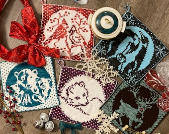 Könnte beinhalten: Satz von sechs gestrickten Topflappen mit verschiedenen Designs. Die Topflappen sind in verschiedenen Farben, darunter Blau, Rot, Grün und Braun. Jeder Topflappen hat ein anderes Design, darunter ein Reh, ein Bär, ein Vogel und eine Schneeflocke.