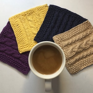 May include: Four knitted coasters in different colors: purple, yellow, navy blue, and beige. The coasters have a cable knit pattern. A white mug with coffee is in the center.