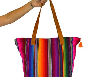 May include: A colorful striped tote bag with brown leather straps and a pink tassel. The bag is made of woven fabric and has a bright, vibrant pattern.