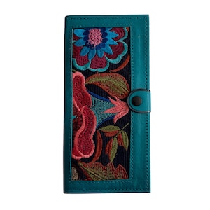 May include: A teal leather wallet with a floral embroidered panel. The embroidery features pink, red, blue, and green flowers on a black background.