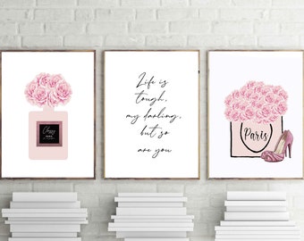 May include: Three white framed prints with pink floral designs. The left print features a pink perfume bottle with a floral design and the text "Classy Paris". The middle print features the text "Life is tough, my darling, but so are you". The right print features a pink shopping bag with the text "Paris" and a pink high heel shoe.