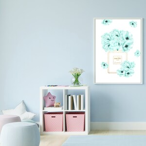 May include: A white framed print with a watercolor illustration of a perfume bottle and light blue flowers. The bottle has gold accents and the text "mon bebe Paris Eau de Parfum" on the label.