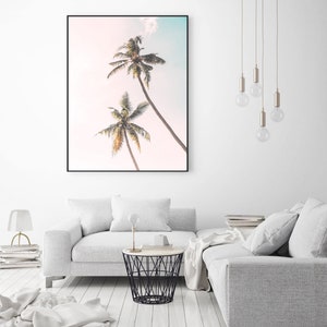 May include: A framed print of two palm trees against a light pink and blue sky. The print is in a black frame and is hanging on a white wall.