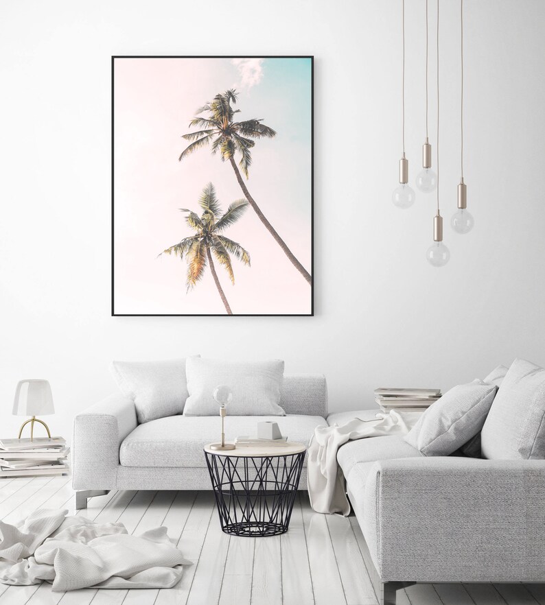 May include: A framed print of two palm trees against a light pink and blue sky. The print is in a black frame and is hanging on a white wall.