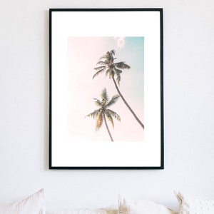 May include: A framed print of two palm trees against a light blue sky. The trees are silhouetted against the sky, with their fronds reaching up towards the top of the frame.