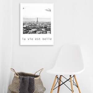 May include: Black and white photograph of the Eiffel Tower and the city of Paris. The photo is framed in a white frame and has the text "la vie est belle" printed below the image.