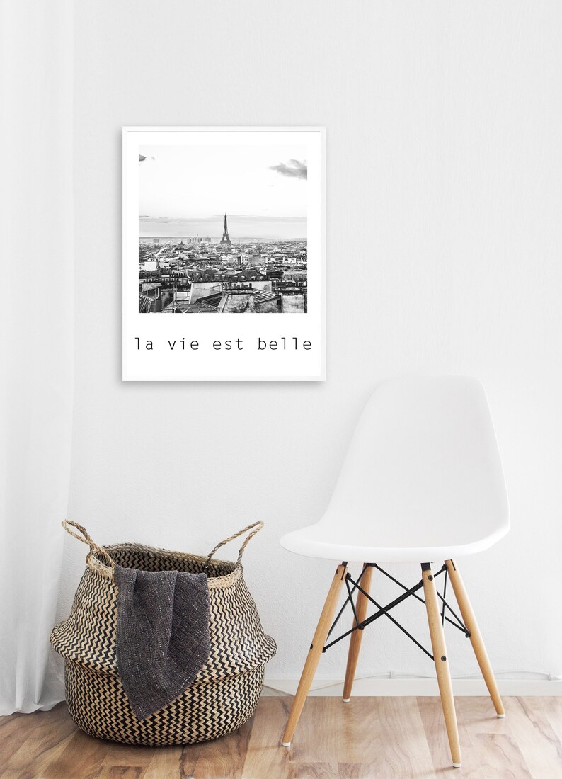 May include: Black and white photograph of the Eiffel Tower and the city of Paris. The photo is framed in a white frame and has the text "la vie est belle" printed below the image.